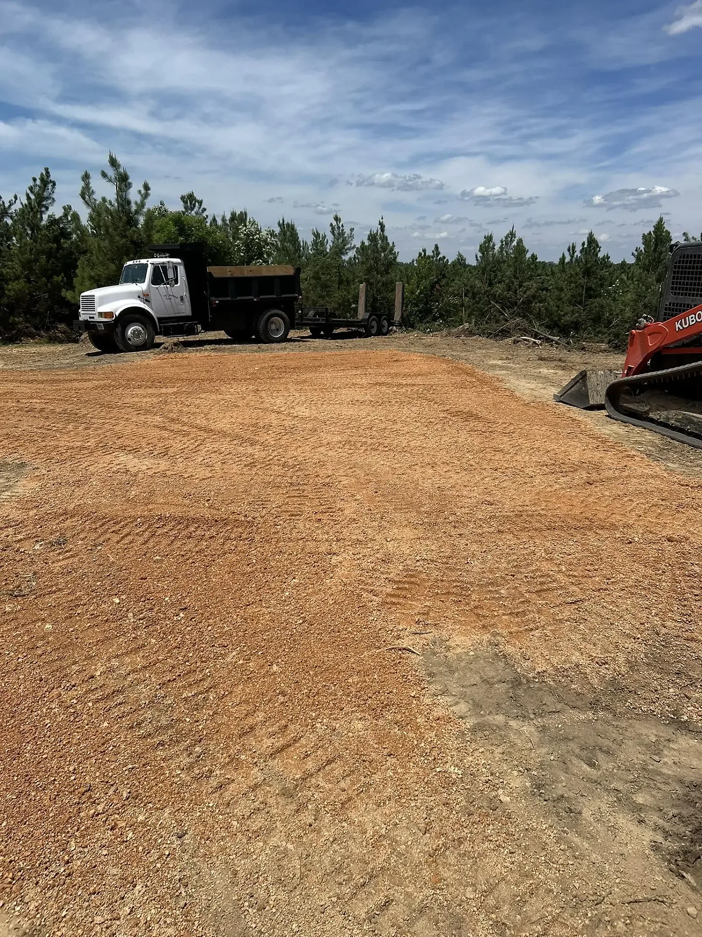 Freshly graded gravel building pad with dump truck and Kubota skid steer on a Dickson, TN jobsite